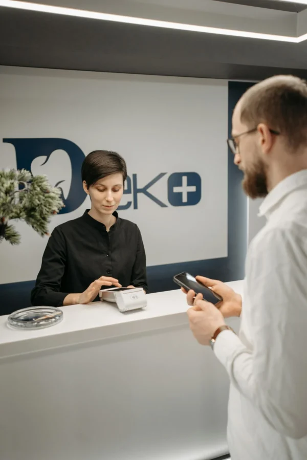 Customer making a cashless payment at a clinic reception using a smartphone and a wireless terminal.