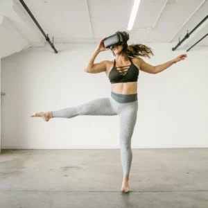 Woman in athletic attire explores virtual reality using a VR headset while dancing in a modern studio.